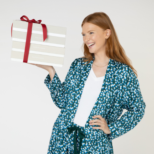 Woman wearing dark green pyjama bottoms and white soft cotton pyjama top with organic cotton robe holding Christmas presents